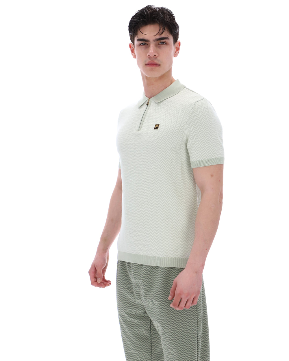 Man wearing a light green polo shirt and patterned pants on a white background
