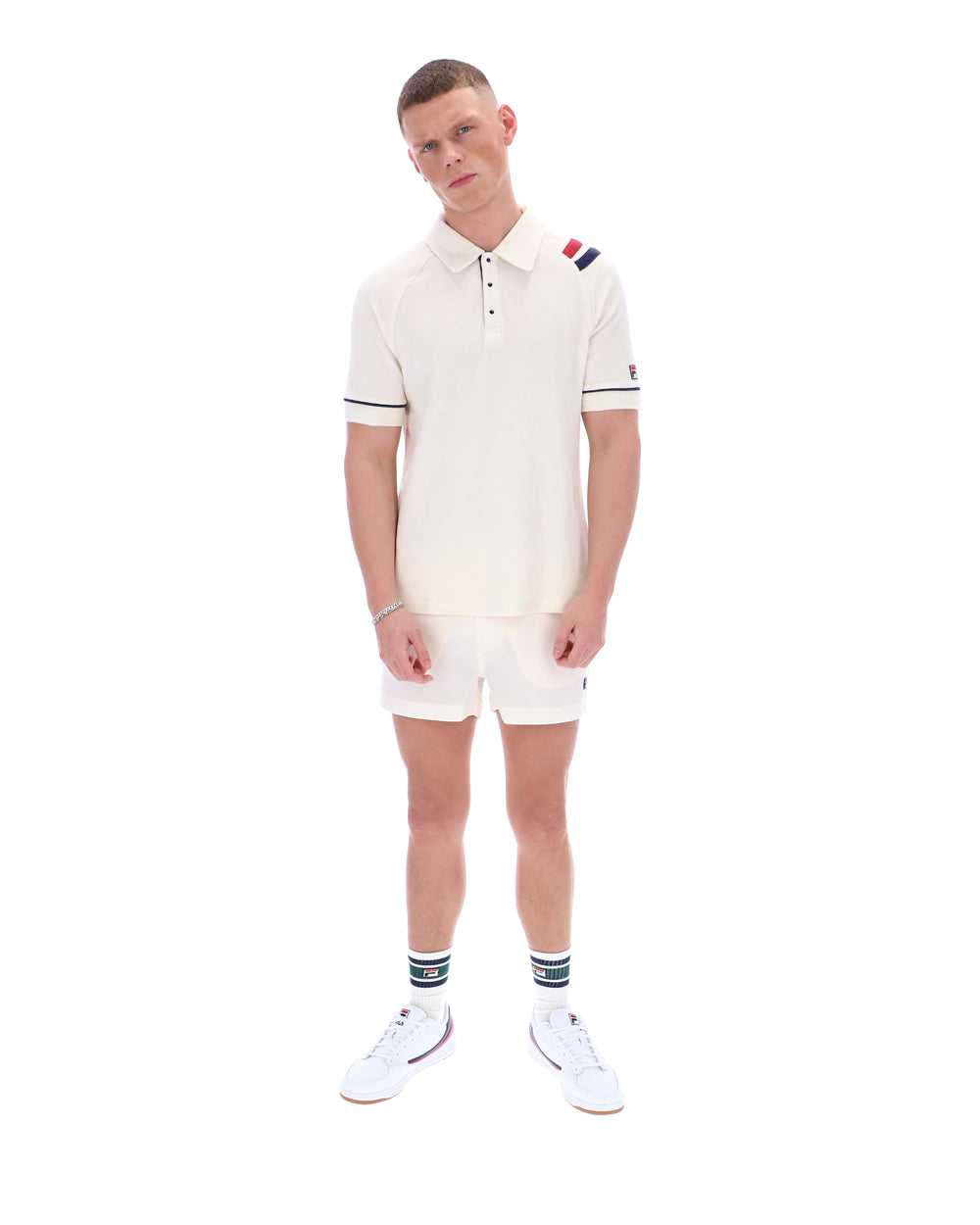 Man wearing a white polo shirt with a FILA logo on the sleeve, paired with matching shorts, on a white background