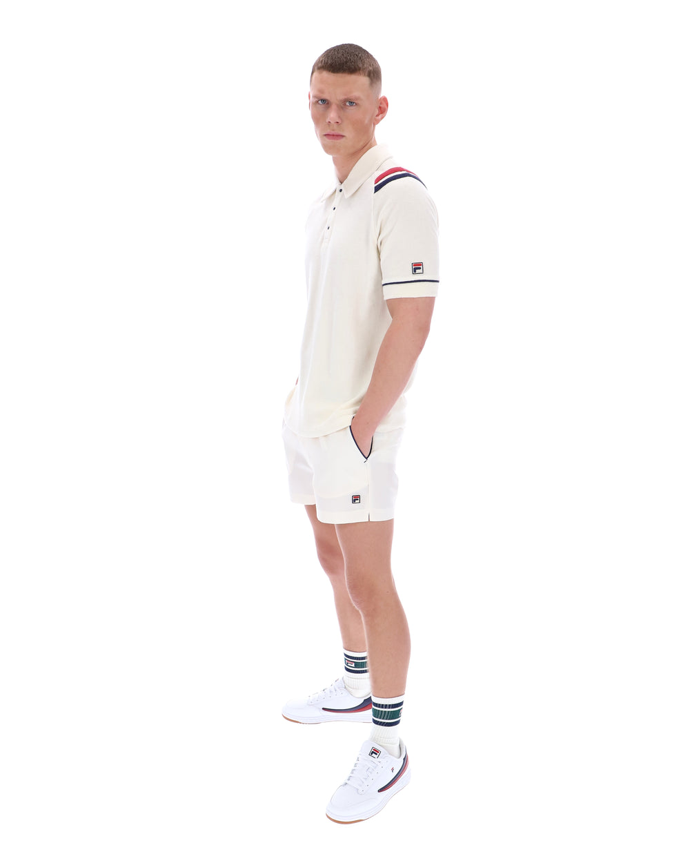 Man wearing a white polo shirt with a FILA logo on the sleeve, paired with matching shorts, on a white background