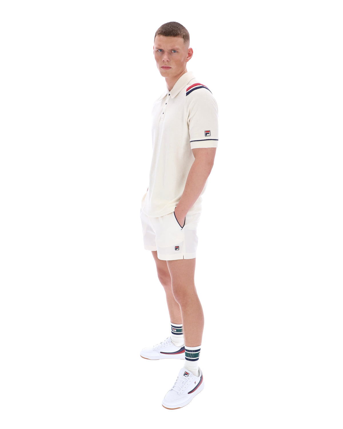 Man wearing a white polo shirt with a FILA logo on the sleeve, paired with matching shorts, on a white background