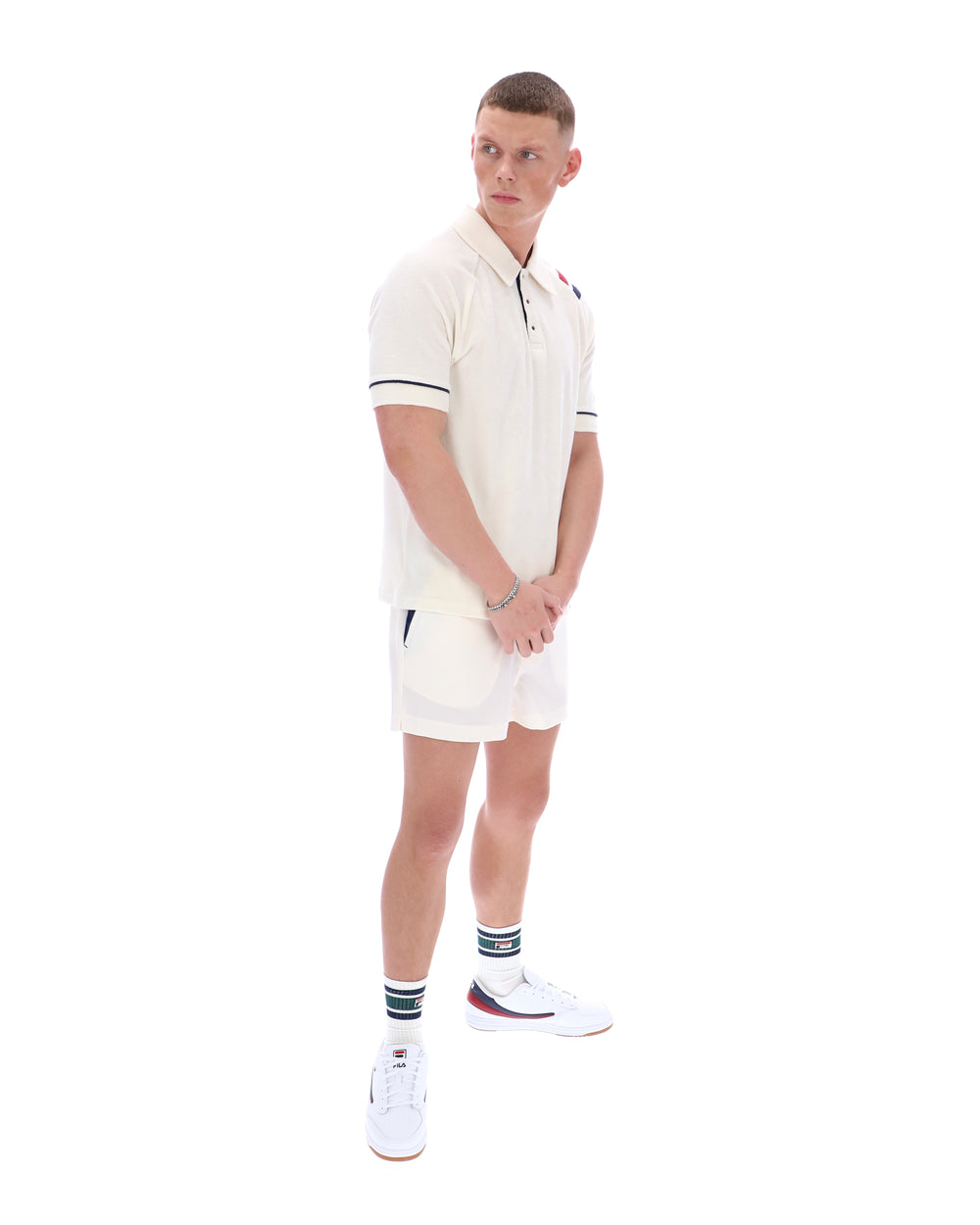 Man wearing a white polo shirt with a FILA logo on the sleeve, paired with matching shorts, on a white background