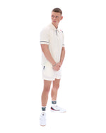 Man wearing a white polo shirt with a FILA logo on the sleeve, paired with matching shorts, on a white background