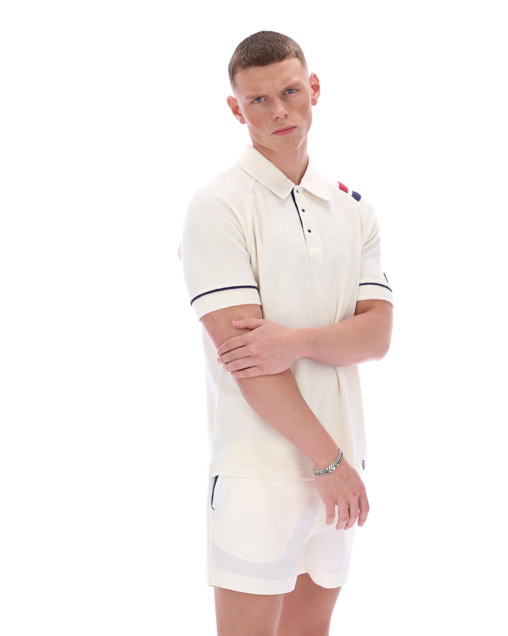 Man wearing a white polo shirt with a FILA logo on the sleeve, paired with matching shorts, on a white background