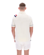 Man wearing a cream polo shirt with a colorful stripe on the sleeve against a white background