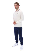 A man modeling a white long-sleeve polo shirt with red and blue striped collar details, navy blue jogger pants, and white sneakers, shown against a plain white background.