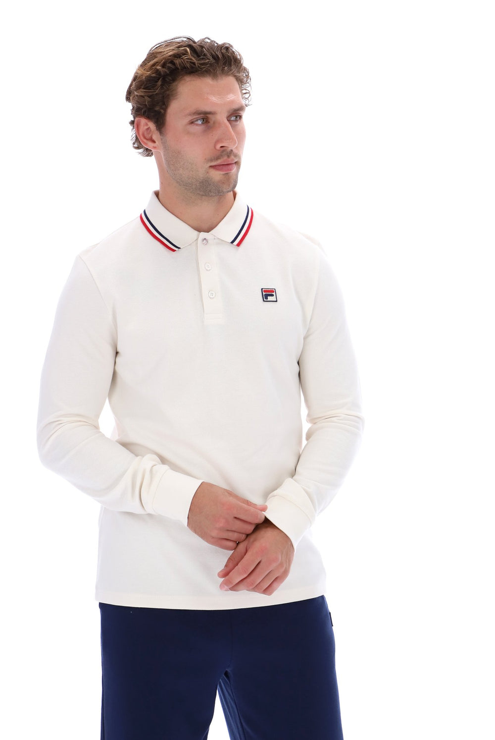 A man wearing a white long-sleeve polo shirt with a red, white, and blue striped collar and a small Fila logo on the chest, paired with navy pants, against a plain white background.
