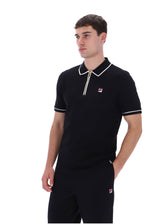 A man wearing a black short-sleeve polo shirt with white trim and a small red and white Fila logo on the chest, paired with matching black trousers, against a plain white background.