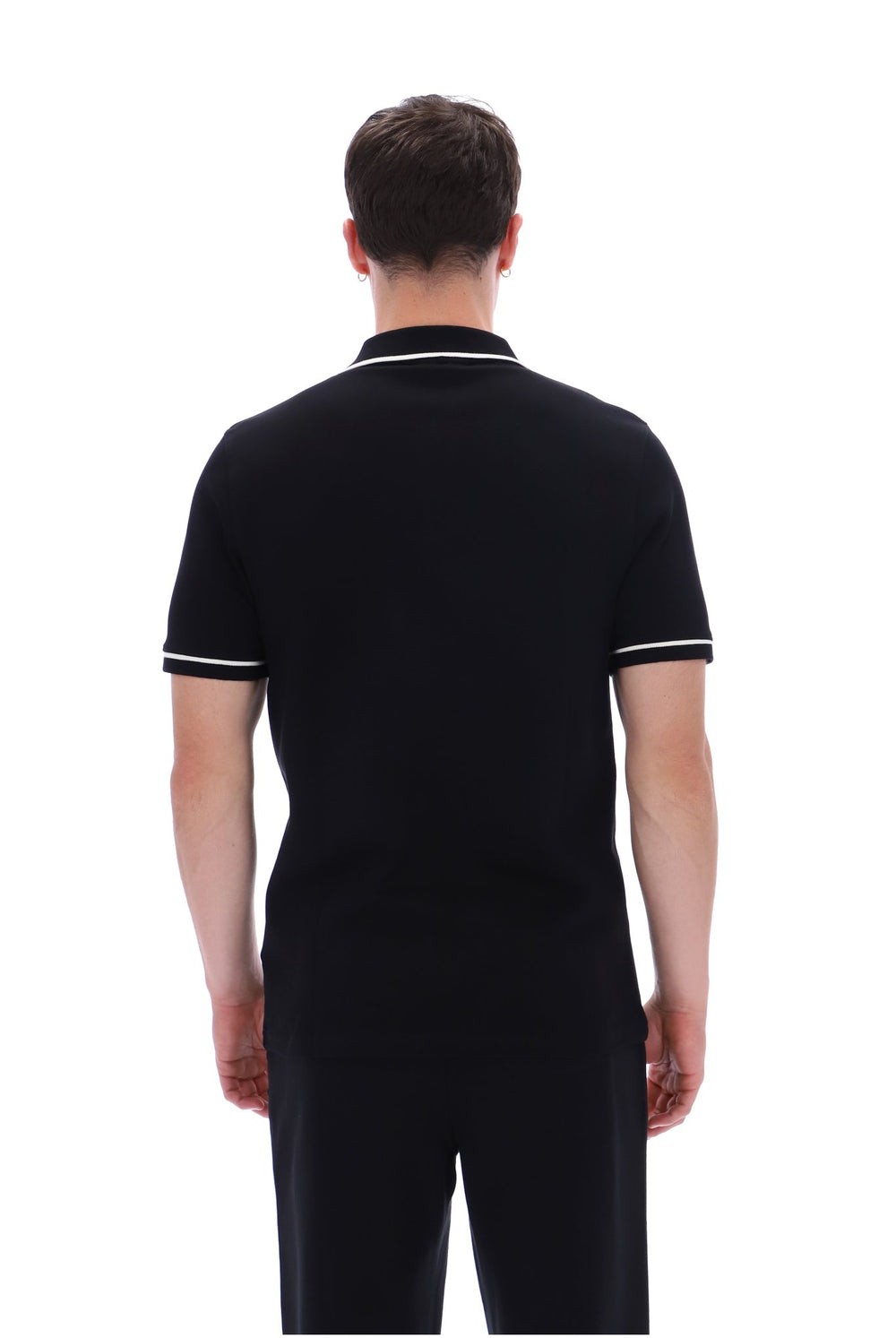 A man viewed from the back wearing a black short-sleeve polo shirt with white piping on the collar and sleeve cuffs, paired with black trousers, against a plain white background.