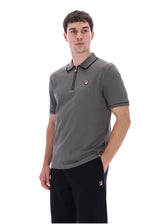 A man wearing a gray short-sleeve polo shirt with a black collar and zipper, featuring a small red, white, and blue Fila logo on the chest, paired with black pants against a white background.