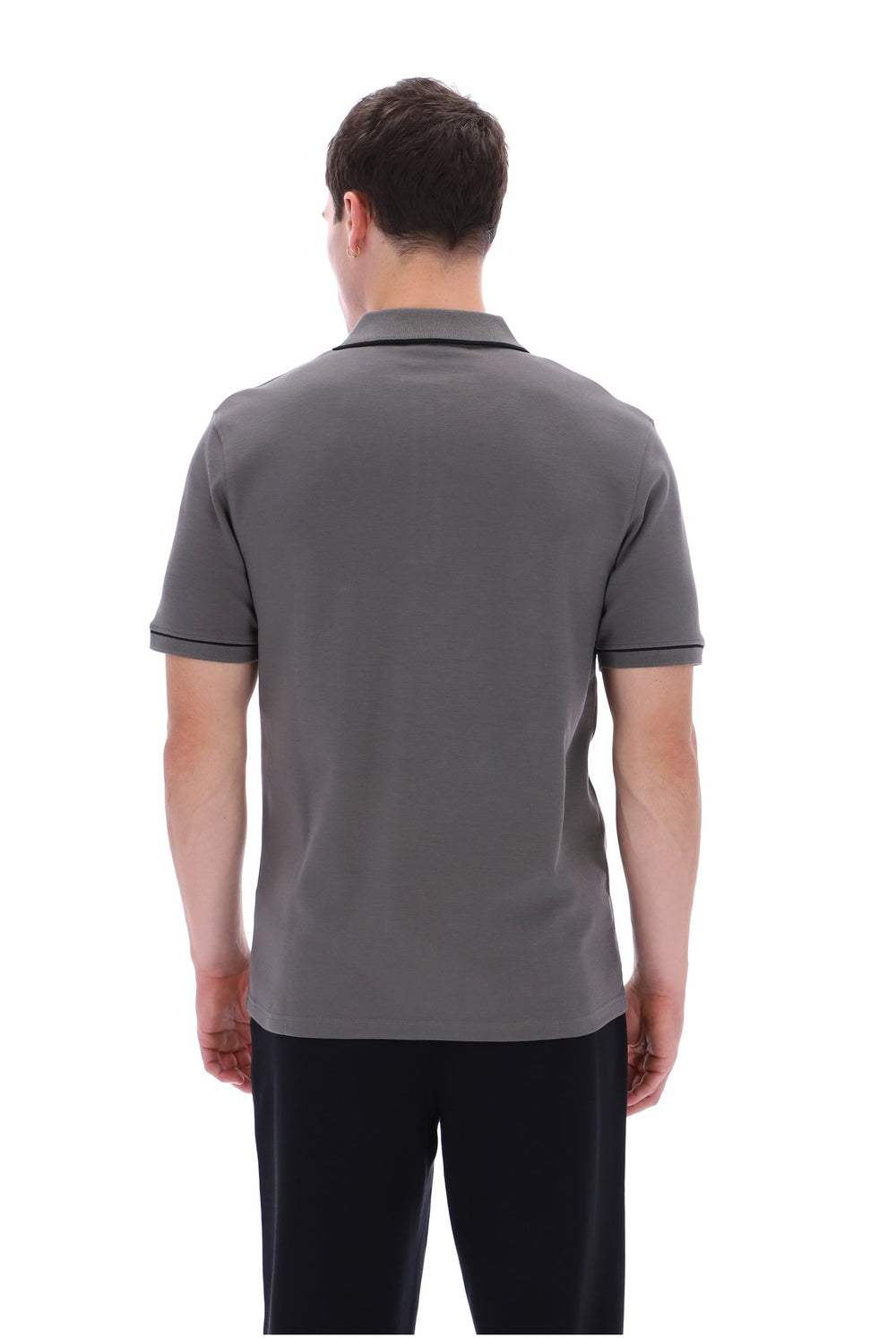 A man viewed from the back wearing a dark gray short-sleeve polo shirt and black pants, standing against a plain white background.