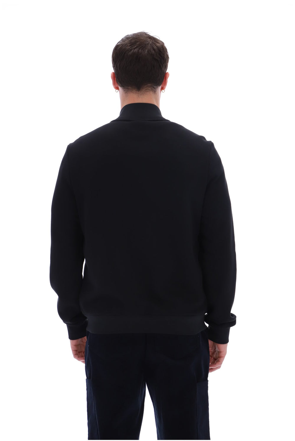 A man viewed from behind wearing a black long-sleeve knit sweater and dark trousers against a plain white background.