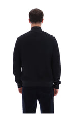A man viewed from behind wearing a black long-sleeve knit sweater and dark trousers against a plain white background.