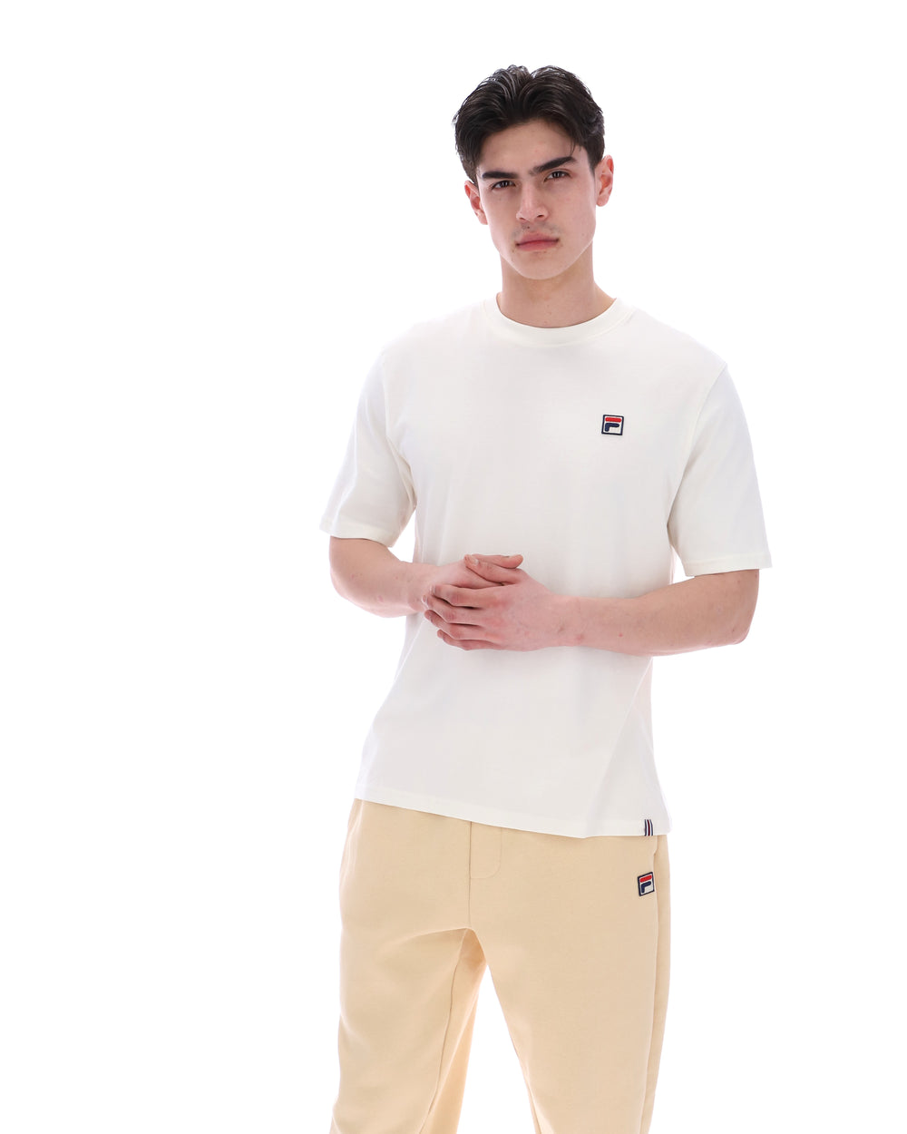 Person wearing a white t-shirt with a small logo and beige pants on a white background