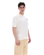 Man wearing a white t-shirt with a small logo on a white background