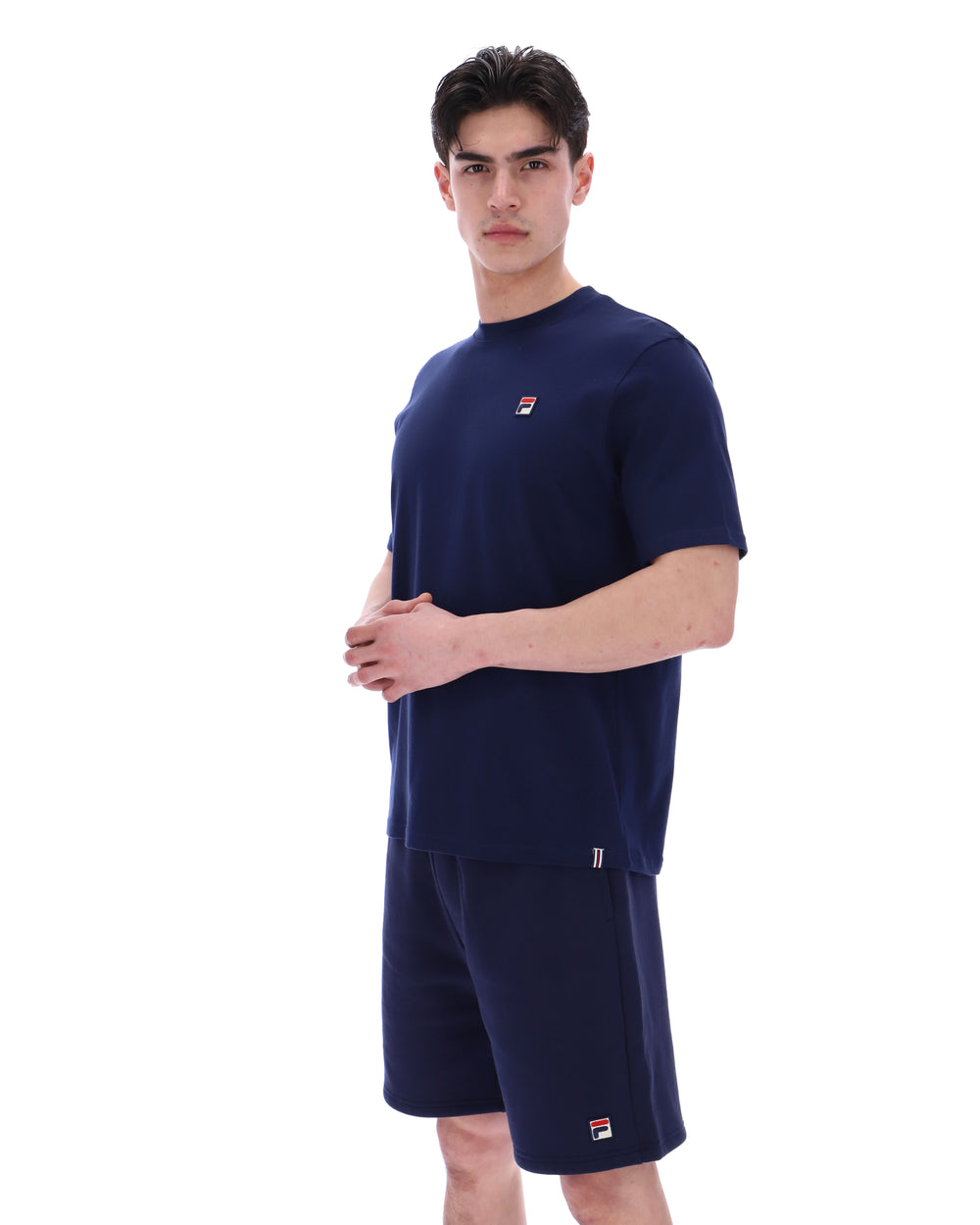 Man wearing a navy blue t-shirt and shorts set with a small FILA logo on a white background