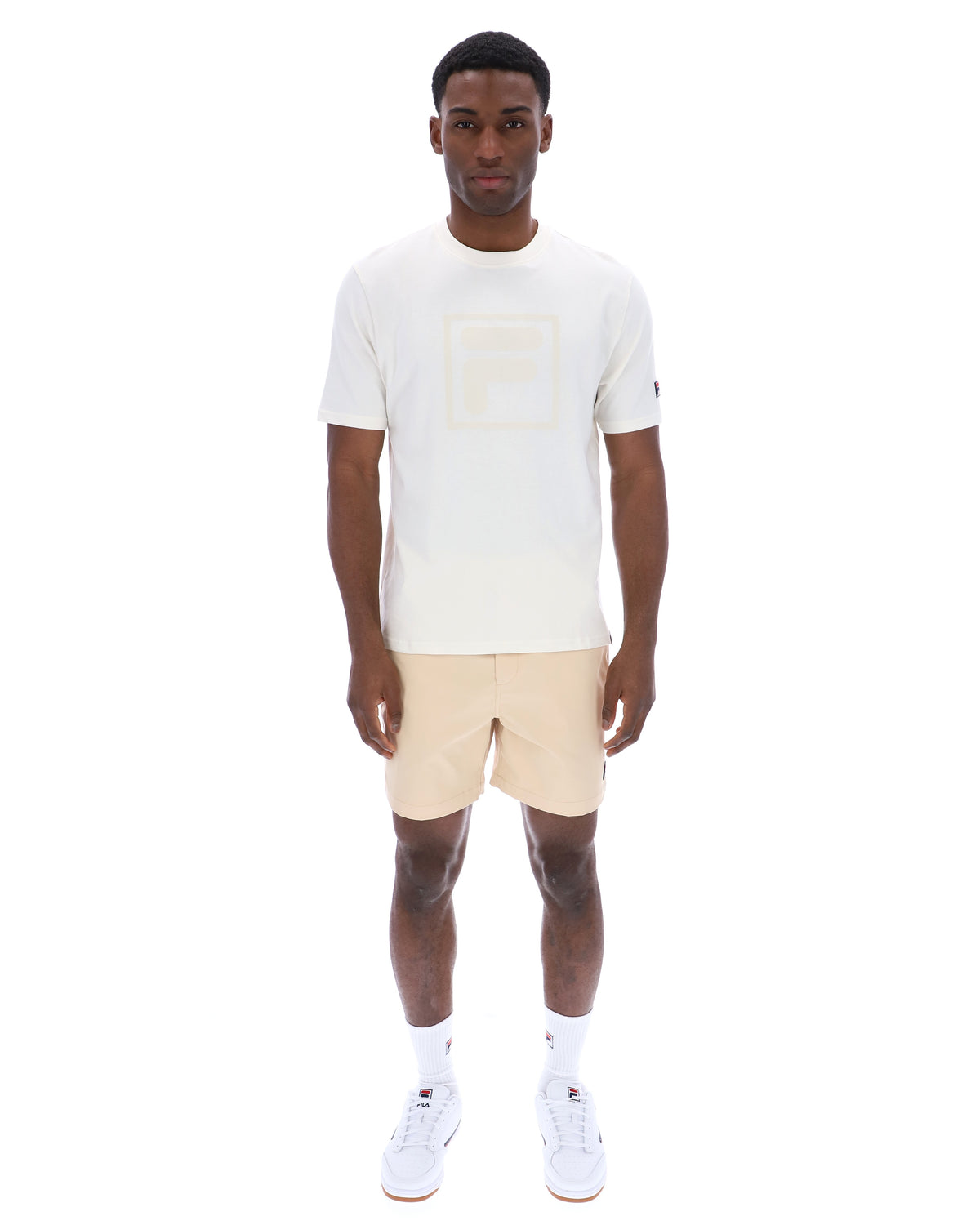 Man wearing a white t-shirt with a cream FILA logo printed on the chest and a classic FILA logo on the sleeve.