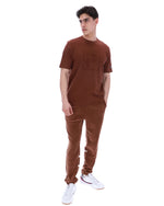 Man wearing a brown t-shirt and pants with white sneakers on a white background