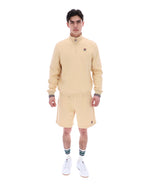 Man wearing a beige tracksuit with a brand logo on a white background