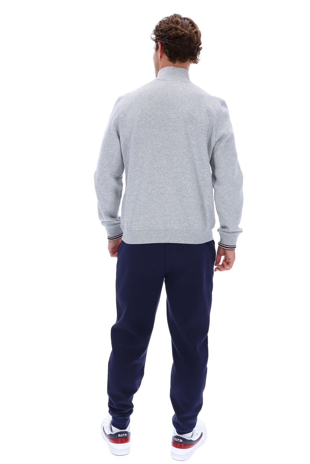 A man viewed from the back wearing a light gray heathered quarter-zip sweatshirt, navy blue sweatpants, and white sneakers with red and blue accents, set against a plain white background.