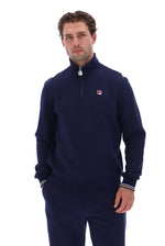 A man wearing a navy blue quarter-zip sweatshirt and matching sweatpants, featuring a small red, white, and blue Fila logo on the left chest, against a solid white background.
