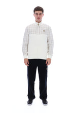 A man modeling a white and beige plaid zip-up jacket with a high collar, paired with black trousers and black sneakers, against a solid white background.