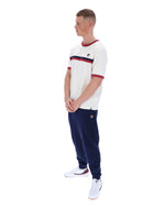 Man wearing a white t-shirt with red and blue stripes and navy tracksuit pants on a white background