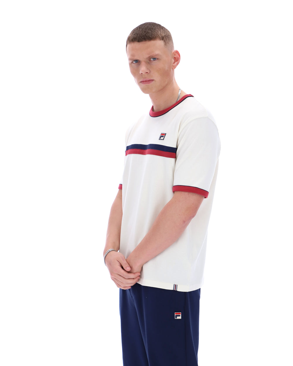 Man wearing a white t-shirt with red and blue accents and dark pants on a white background