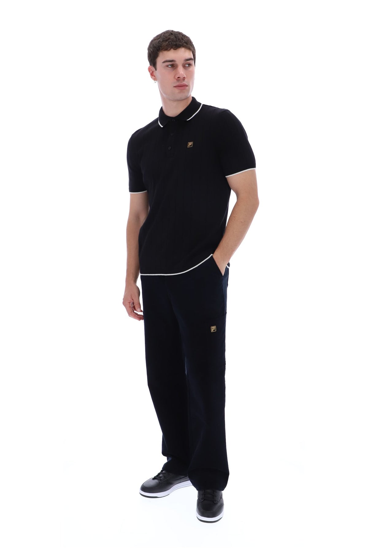A man modeling a black short-sleeve polo shirt and matching black sweatpants with white piping and small gold embroidered logos, set against a plain white background.
