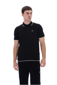 A man wearing a black short-sleeve polo shirt with white piping and a small gold embroidered logo on the chest, paired with black pants, against a plain white background.