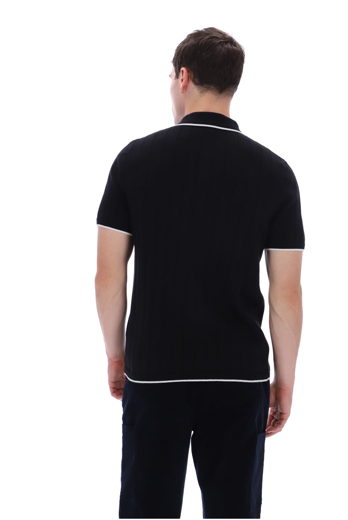 A man viewed from behind wearing a black short-sleeve knit polo shirt with white contrast piping on the collar, sleeve cuffs, and hem, paired with dark trousers, against a plain white background.