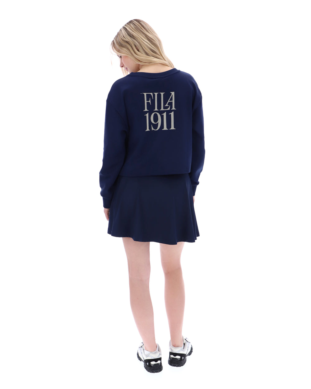 Person wearing a navy blue sweater and skirt with 'FILA 1911' logo on a white background