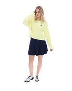 Woman wearing a yellow long-sleeve top and navy skirt on a white background