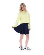 Woman wearing a yellow long-sleeve top and navy skirt on a white background