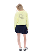 Person wearing a light yellow 'Fila 1911' sweatshirt and dark blue skirt on a white background