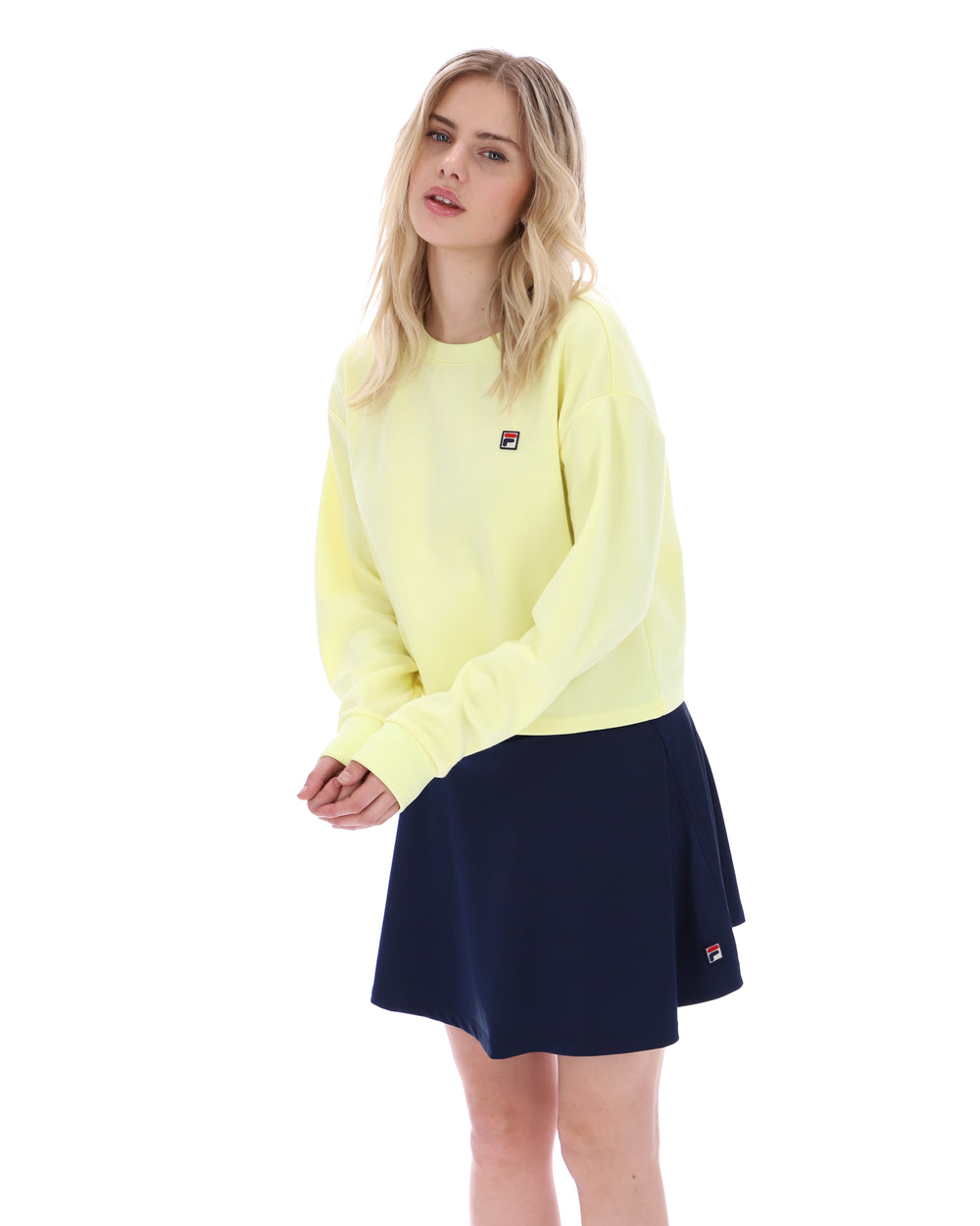 Woman wearing a yellow sweater and navy skirt on a white background