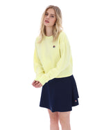 Woman wearing a yellow sweater and navy skirt on a white background