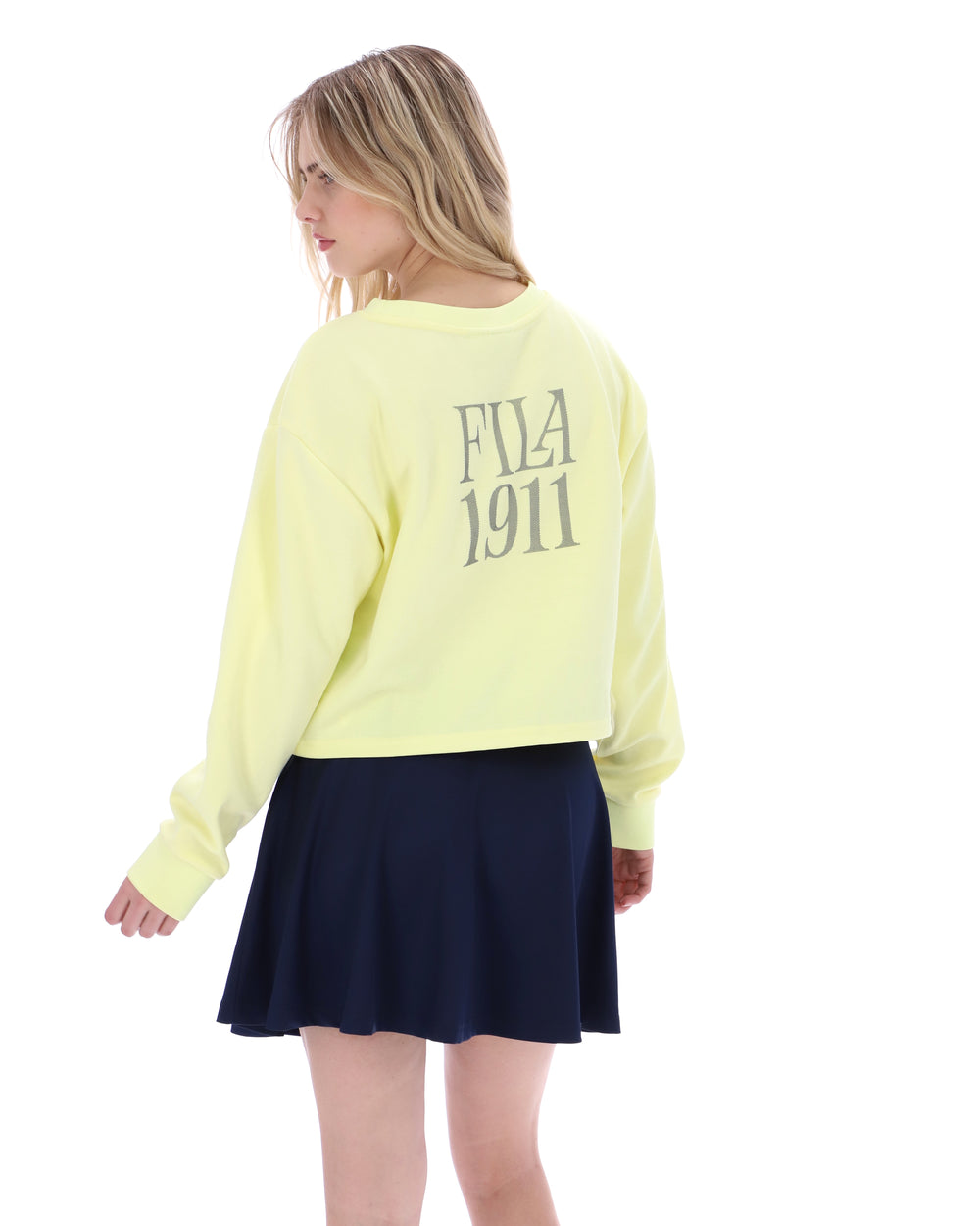 Person wearing a light yellow sweatshirt with 'Fila 1911' logo and a navy skirt on a white background