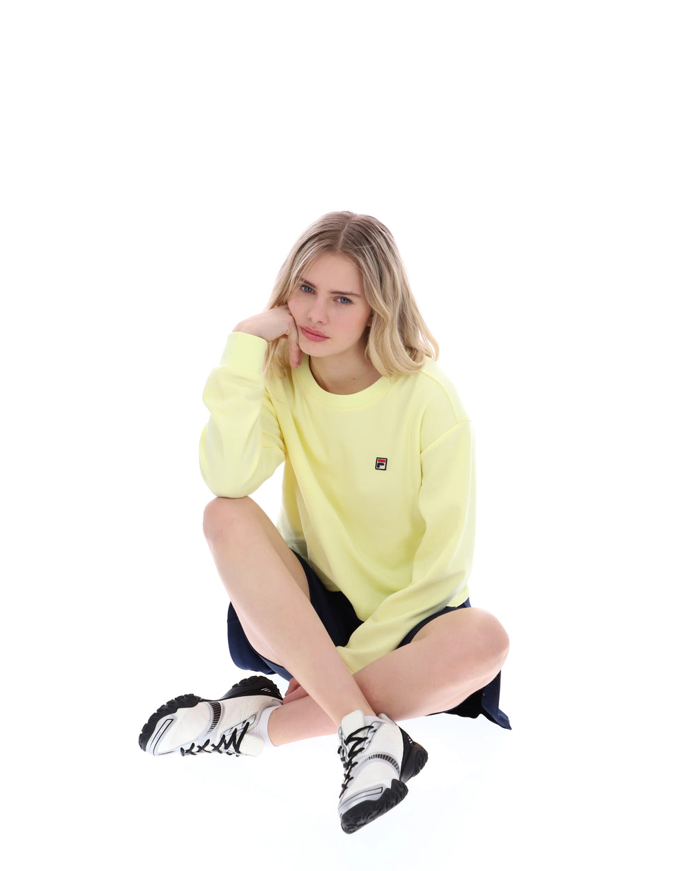 Woman wearing a yellow sweatshirt sitting on a white background