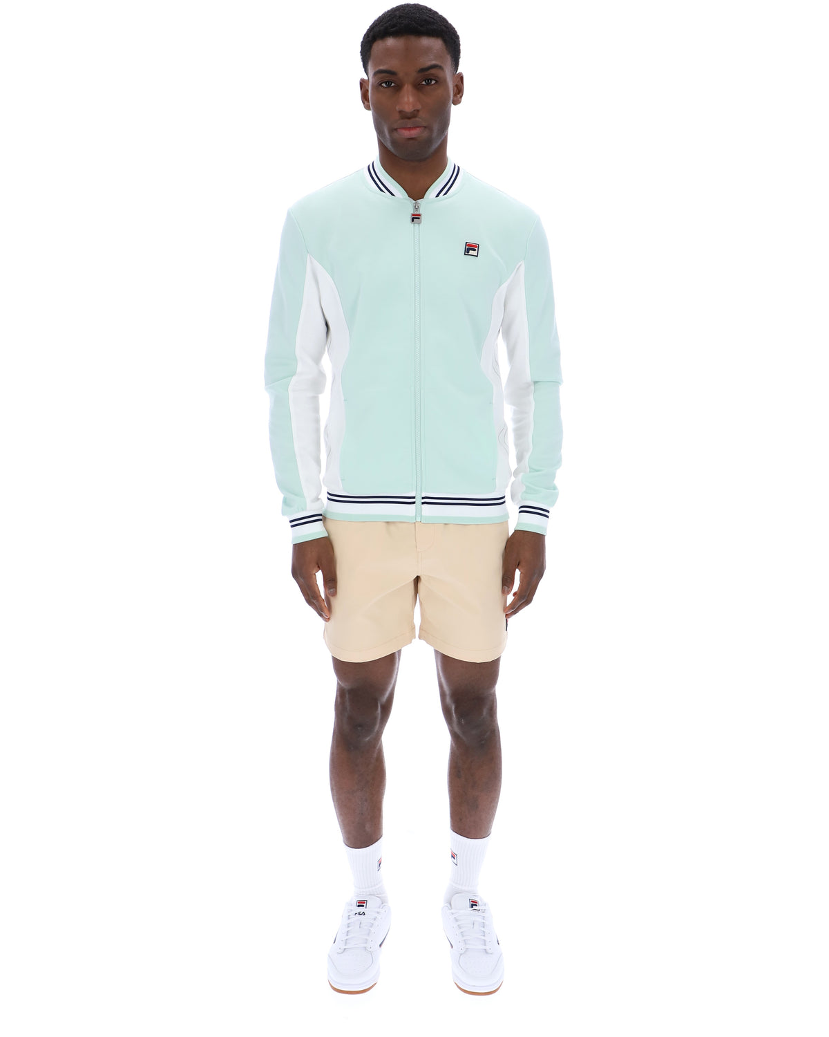 Man wearing a light blue jacket with white accents and beige shorts on a white background