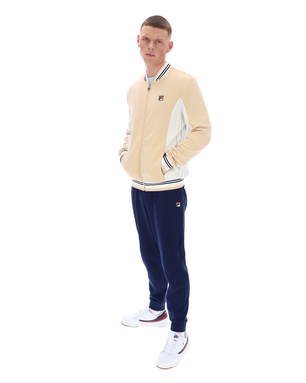 Man wearing a beige tracksuit with navy pants on a white background