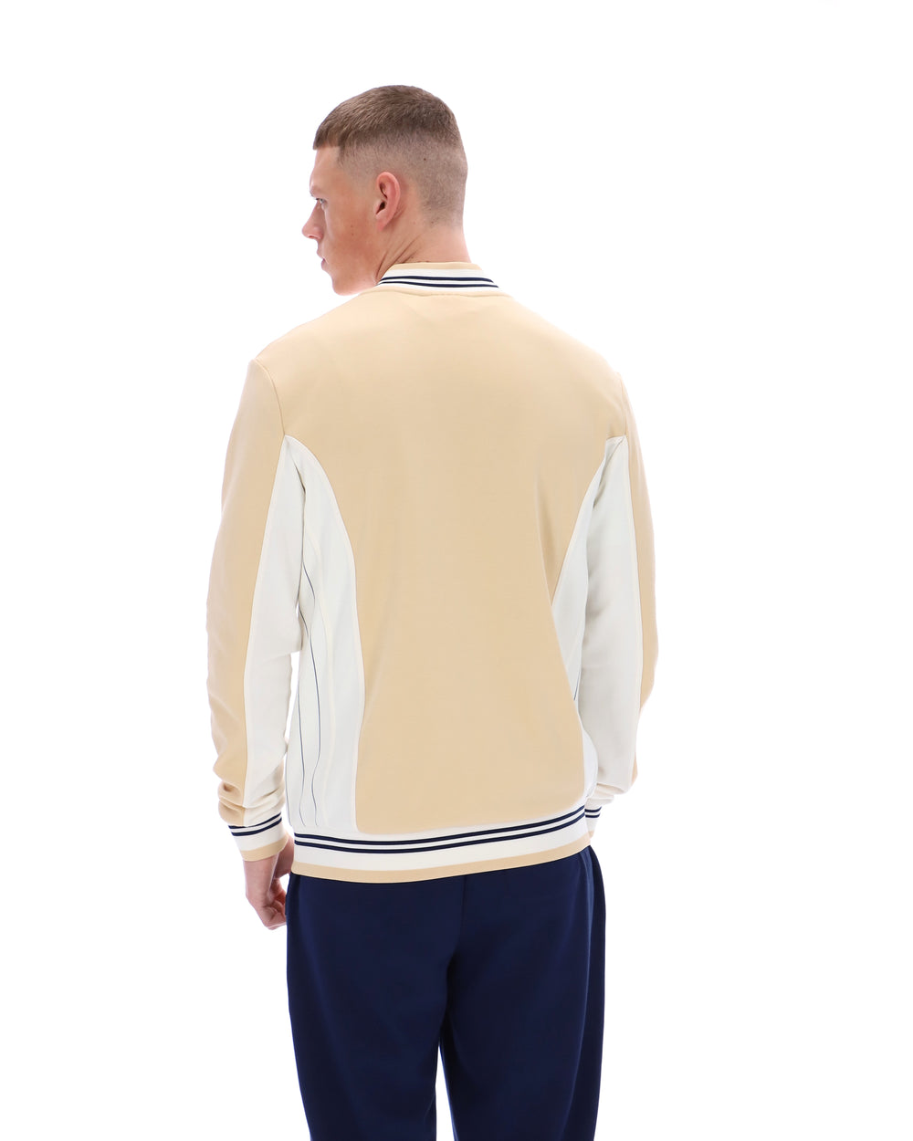 Man wearing a beige and white varsity jacket with navy pants on a white background
