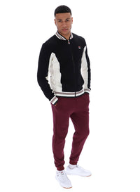 Man wearing a black and white tracksuit with maroon pants on a white background
