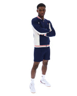 Man wearing a navy tracksuit with white accents on a white background