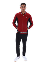 A man modeling a red and black zip-up bomber jacket with white and black striped ribbed collar, cuffs, and hem, paired with black pants and white sneakers against a plain white background.