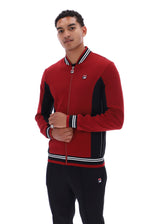 A man wearing a red and black Fila zip-up track jacket with white stripe details on the collar, cuffs, and hem, paired with black track pants, against a plain white background.