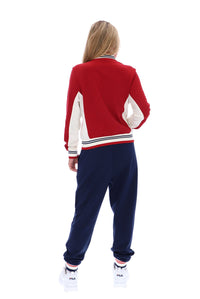 A woman shown from the back wearing a red varsity-style jacket with cream sleeves and navy jogger pants, paired with white sneakers, on a plain white background.