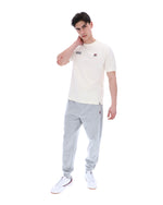 Man wearing a white t-shirt with a FILA logo on the left side of the chest, and 'EST 1911' text on the right side of the chest. Paired with grey joggers, against a white background