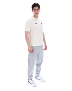 Man wearing a white t-shirt with a FILA logo on the left side of the chest, and 'EST 1911' text on the right side of the chest. Paired with grey joggers, against a white background
