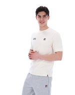 Man wearing a white t-shirt with a FILA logo on the left side of the chest, and 'EST 1911' text on the right side of the chest. Paired with grey joggers, against a white background