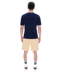 Man wearing a navy blue t-shirt with a FILA logo on the left side of the chest, and 'EST 1911' text on the right side of the chest. Paired with a beige shorts, against a white background